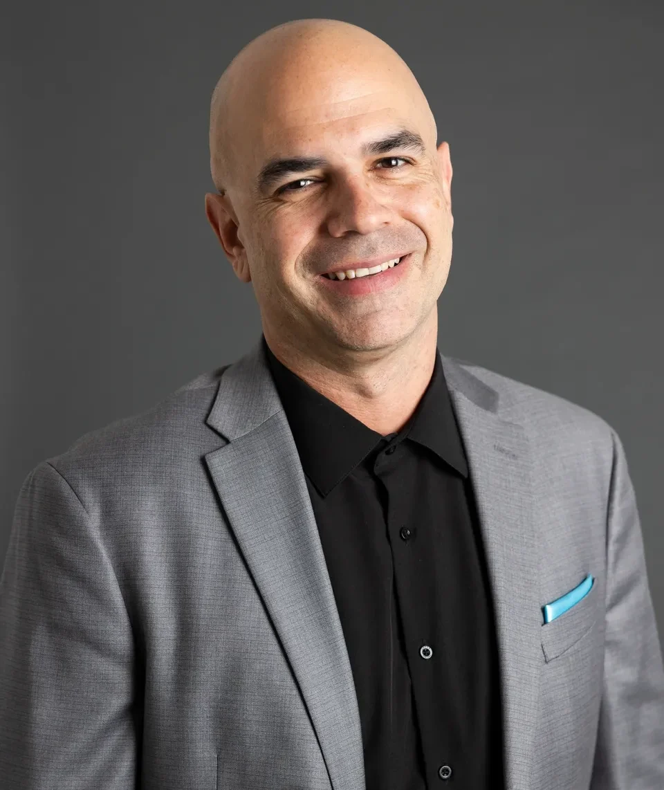 Smiling bald man in gray suit and black shirt.